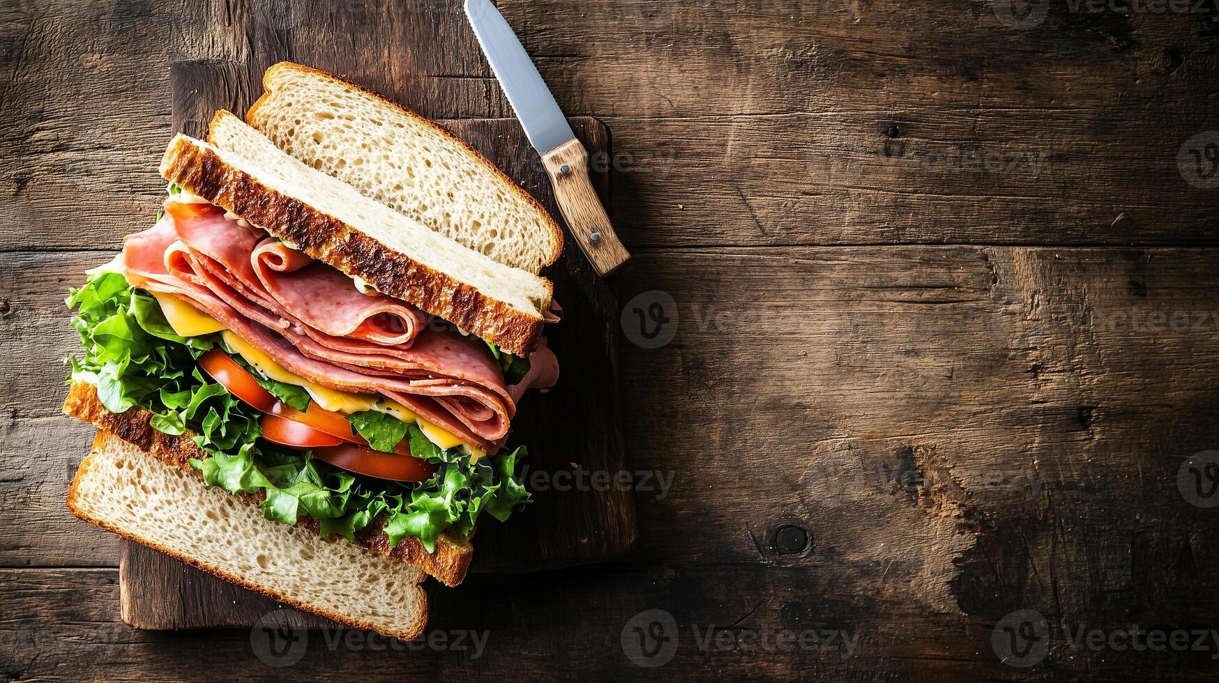 Classic deli sandwich sliced open on a wooden surface beside a butter knife, food setting photo