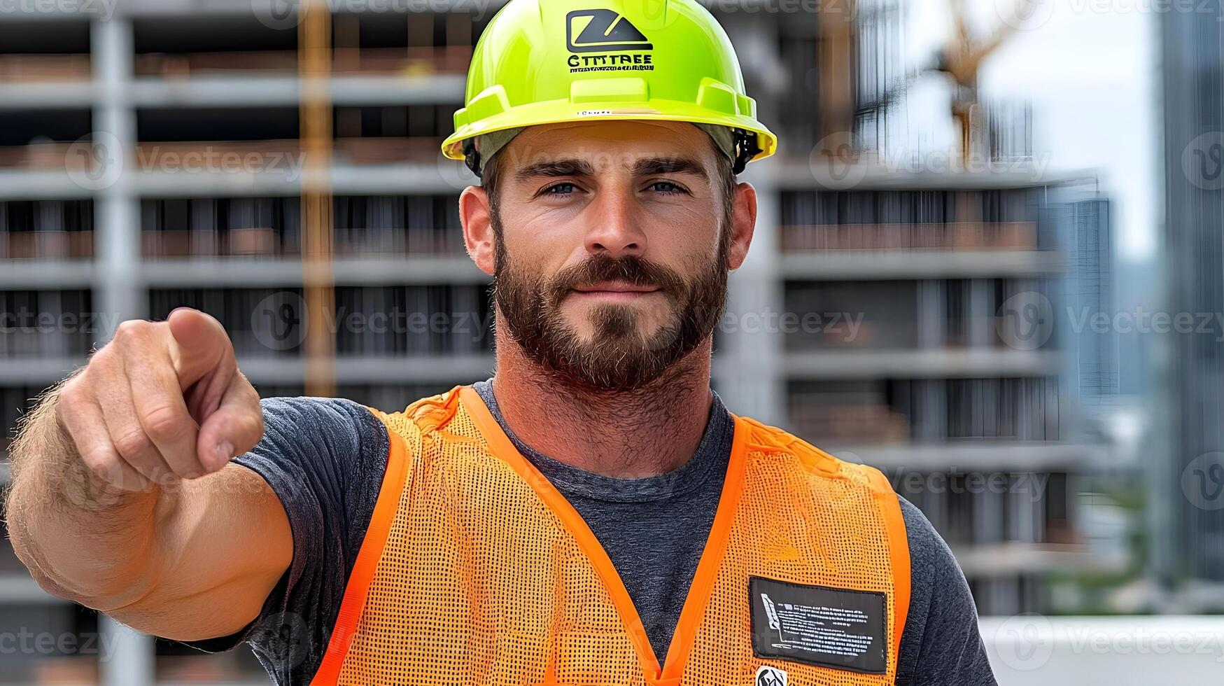 Confident construction worker in hard hat pointing to the camera at a building site with modern structures under construction in the background photo