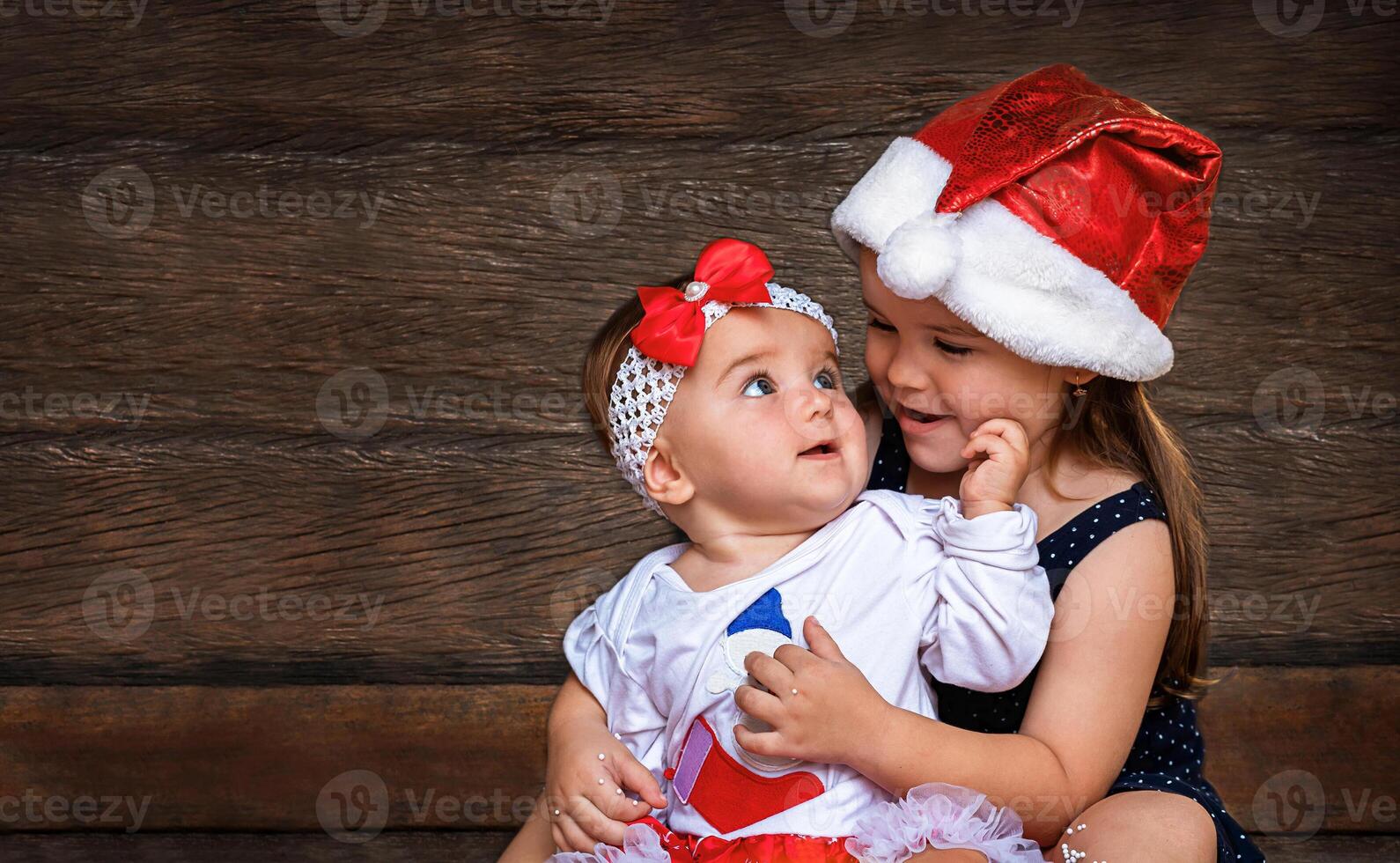 children in Christmas Santa caps on the wooden background. Older sister cares holding younger photo