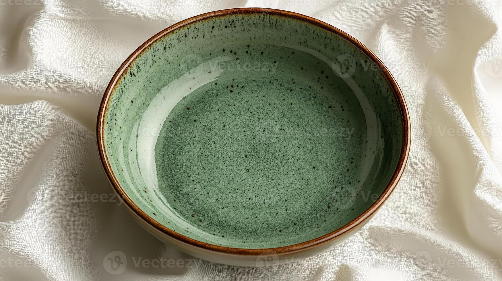 Beautiful handcrafted ceramic bowl with a green glaze resting elegantly on soft fabric in a serene setting photo