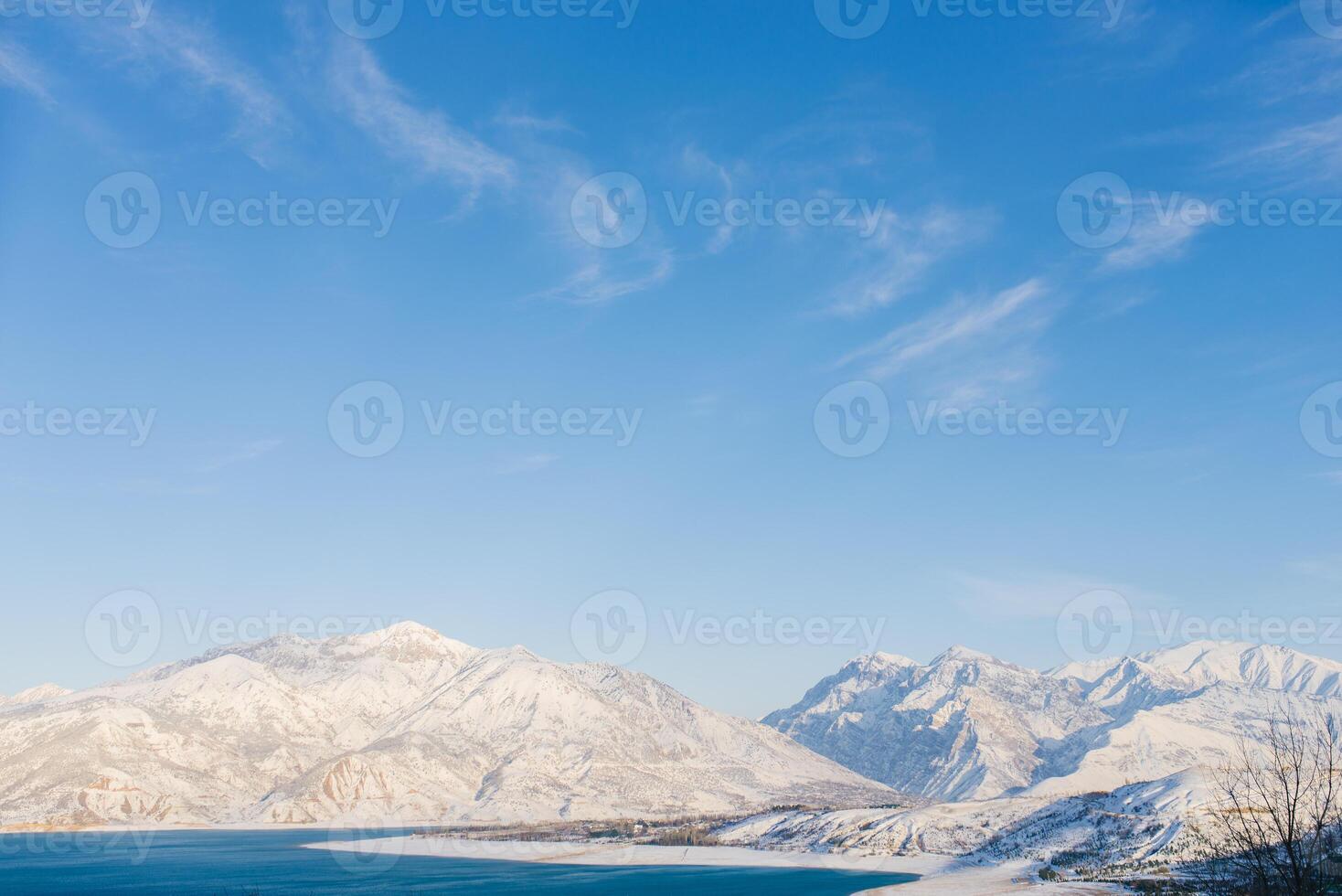 Charvak reservoir with blue water on a clear winter day in Uzbekistan, surrounded by snow-capped mountain peaks of Tien Shan photo