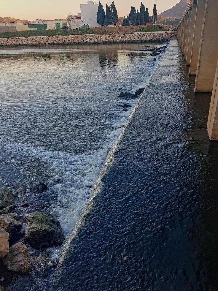 A wide waterfall current under a bridge in Wadi. Close to flowing water, discover complex details photo