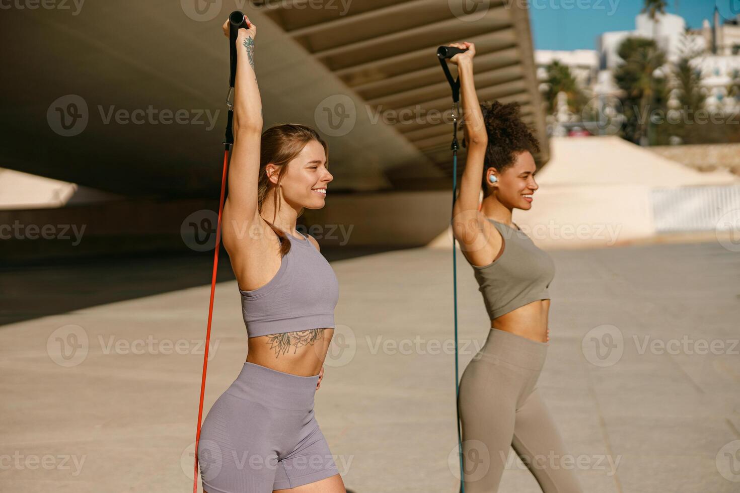 Two fitness women doing exercise with resistance elastic band outside in urban environment photo