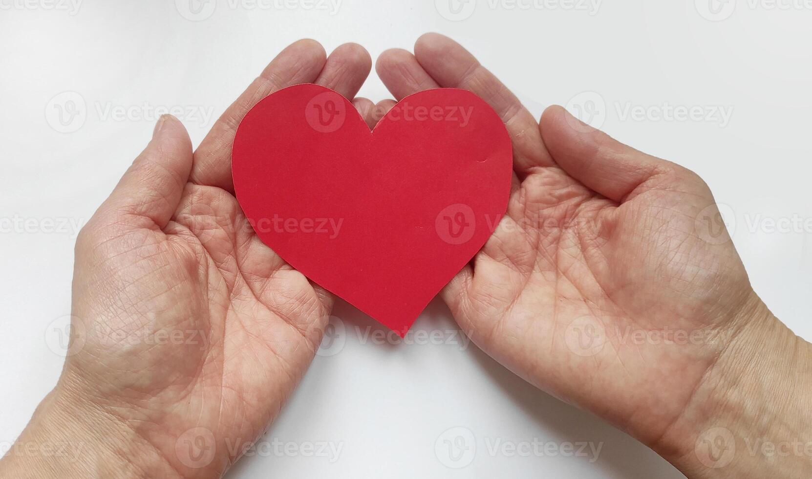 Top view of female hands holding red empty heart shaped paper card on white background. Valentine's day, health, healthy heart care photo