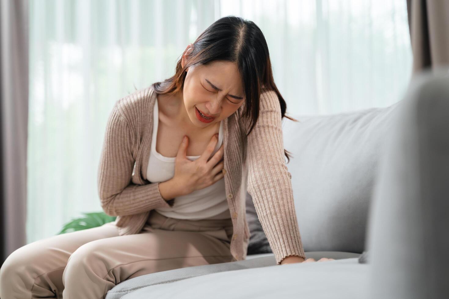 A woman is sitting on a couch with her hand on her chest. Healthcare and medical concept. photo