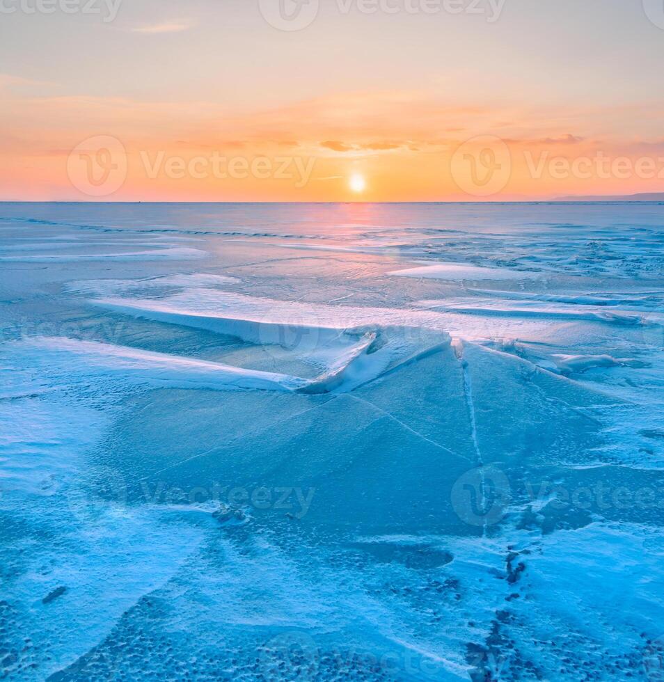Winter landscape. A frozen surface of ice with snow intersected by many cracks. photo