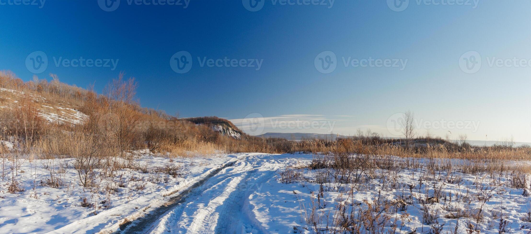 Winter landscape. Road covered with snow and a hill with tall dry grass on a sunny day. photo