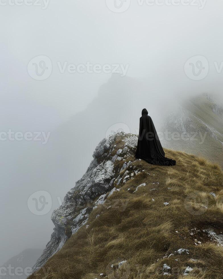 Mysterious figure in cloak standing on a foggy mountain peak photo