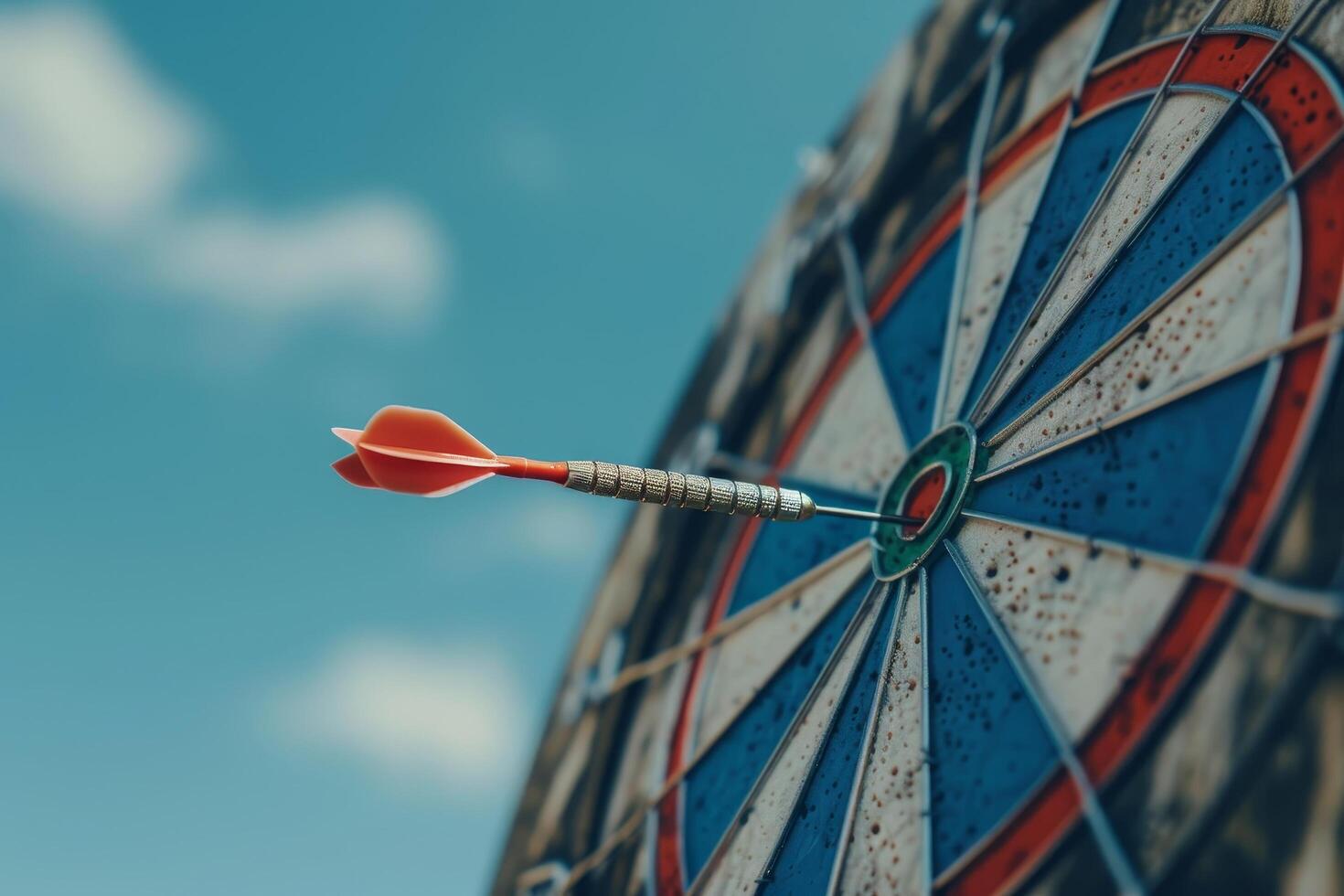 Dart hitting the bullseye on a dartboard against a blue sky photo