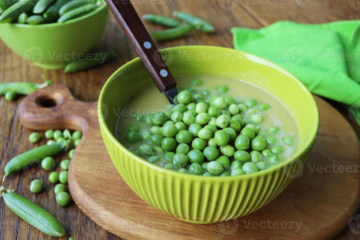 Fresh green pea soup with pea seeds and pea pods around . Selective Focus, Focus on the pea in the middle of the soup photo