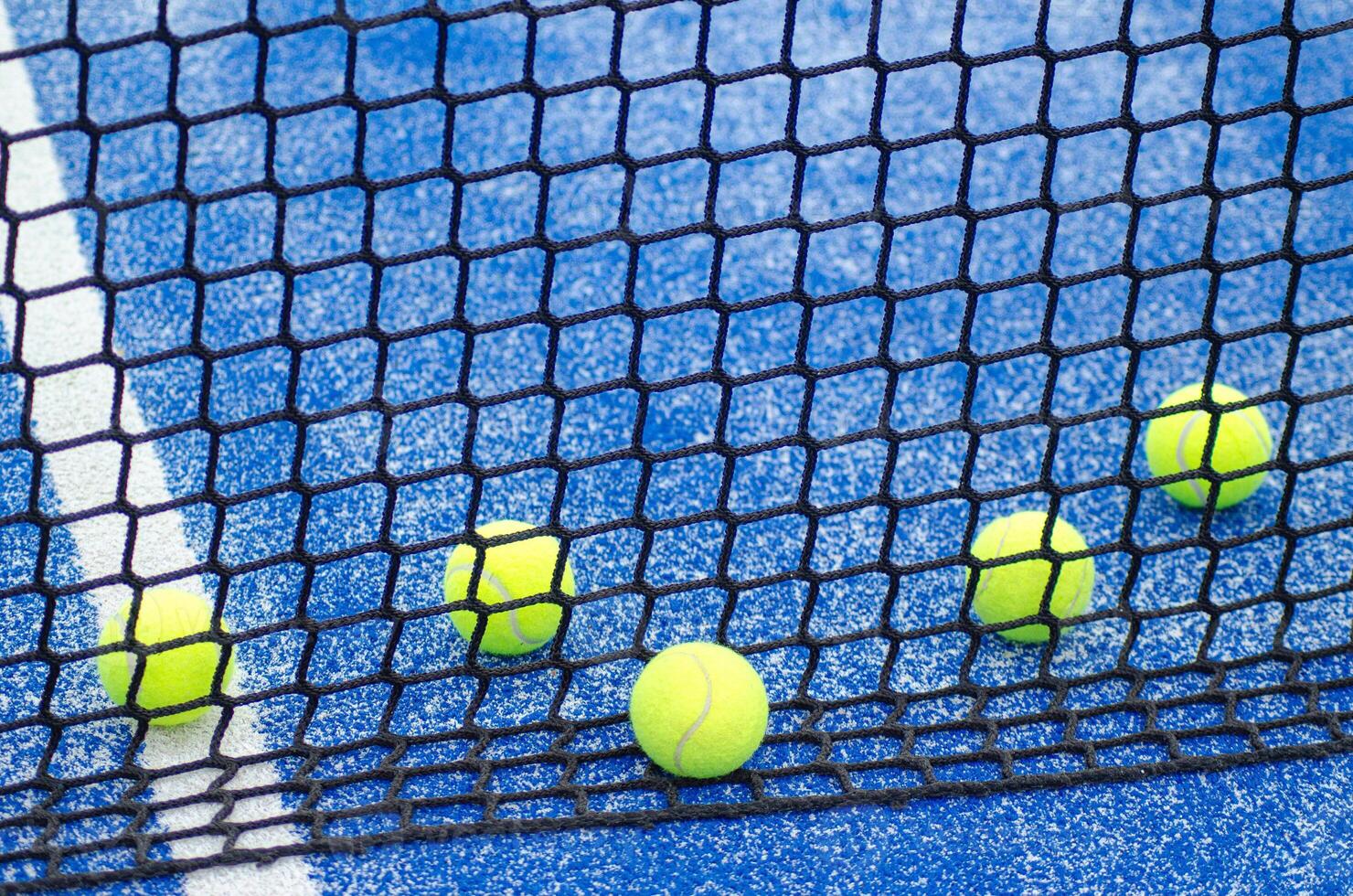 five balls near the net in a blue paddle tennis court photo