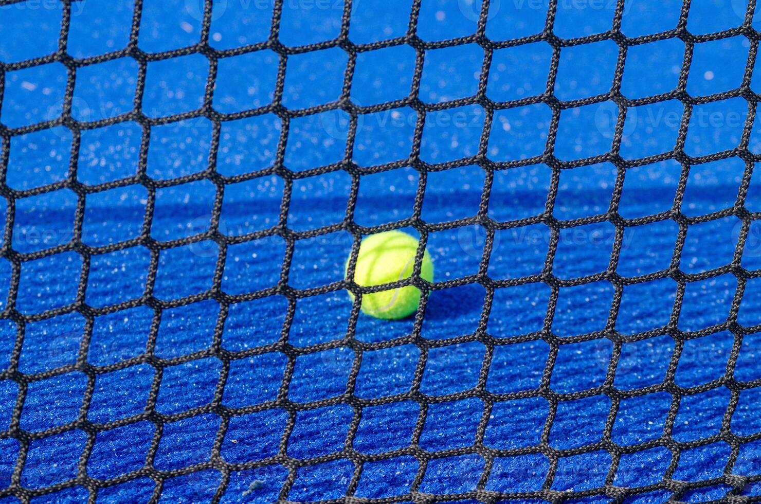 Selective focus, isolated ball on a paddle court, with the net out of focus in the foreground. photo