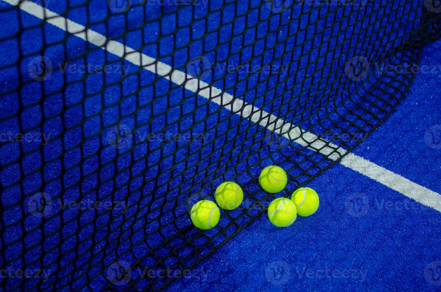 Net of a blue paddle tennis court and five balls. photo