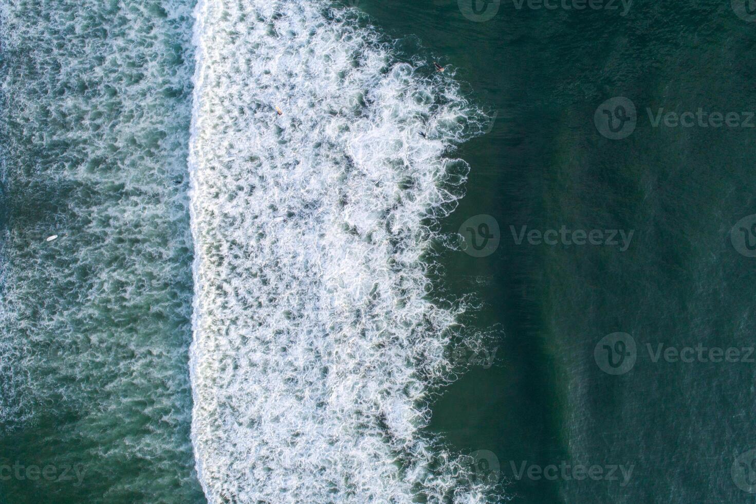 view of a wave on the shore of a beach at sunrise, and people surfing. Aerial top view photography with a drone. photo