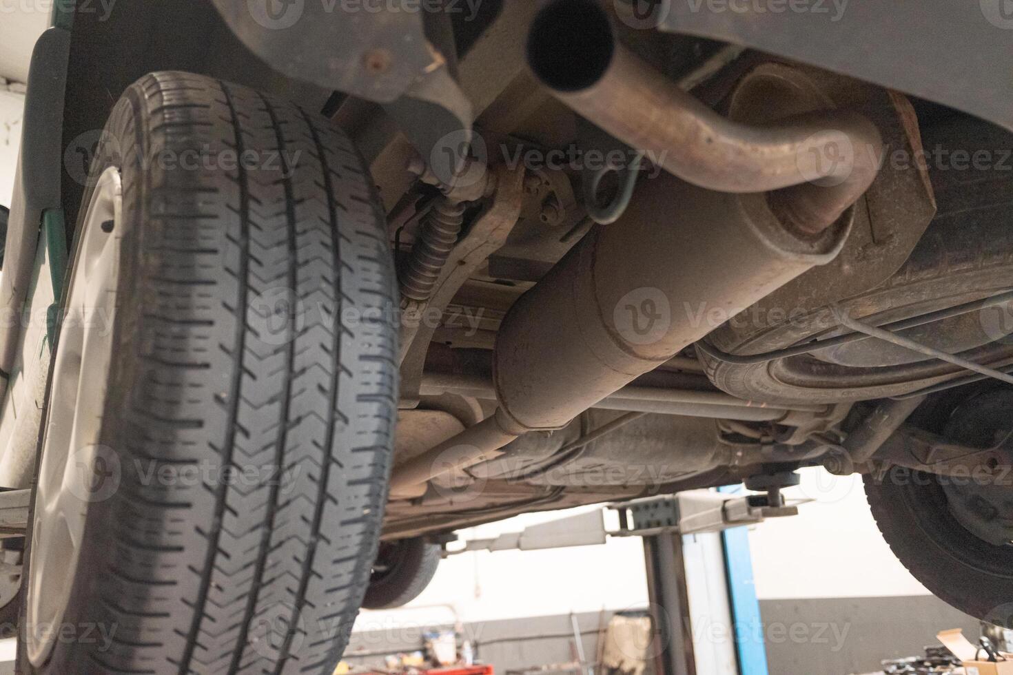 Underside view of car lifted on hydraulic lift in auto repair shop for maintenance and inspection. Vehicle in garage setting ready for work. photo