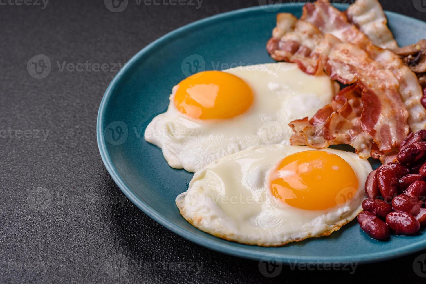 English breakfast with fried eggs, bacon, beans, tomatoes, spices and herbs photo