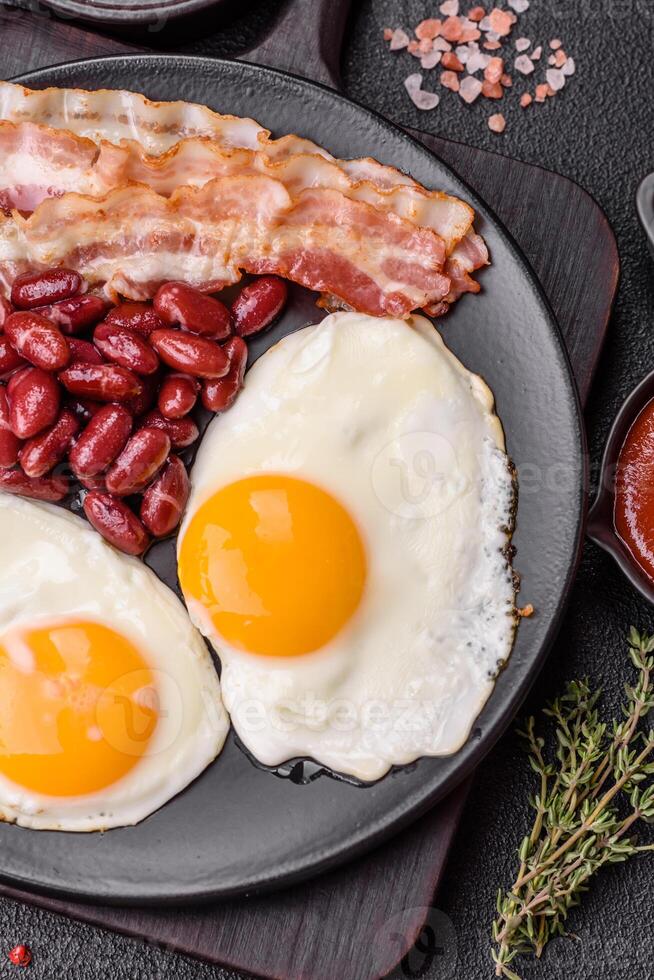 English breakfast with fried eggs, bacon, beans, tomatoes, spices and herbs photo
