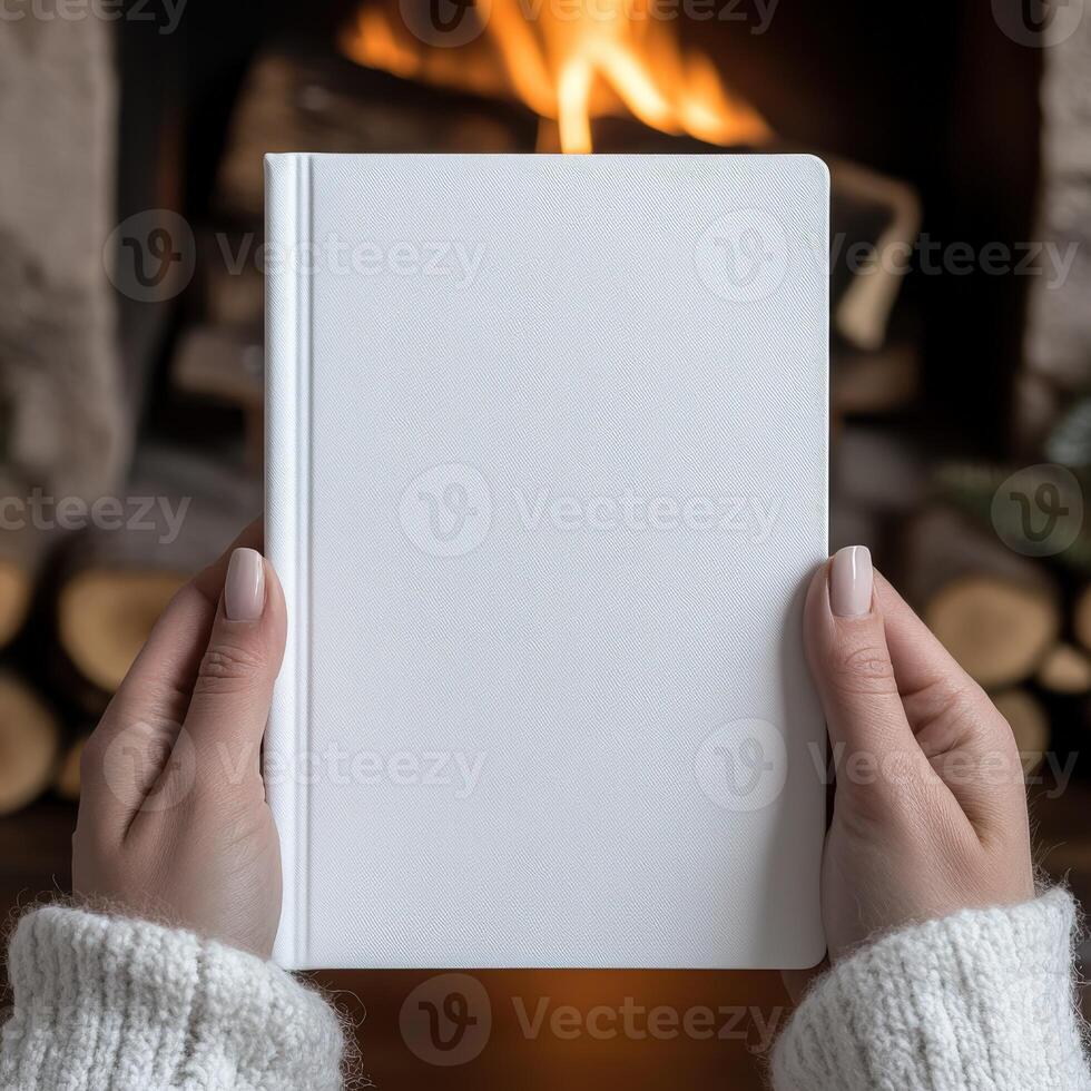 Cozy hands hold a blank notebook near a warm fireplace photo