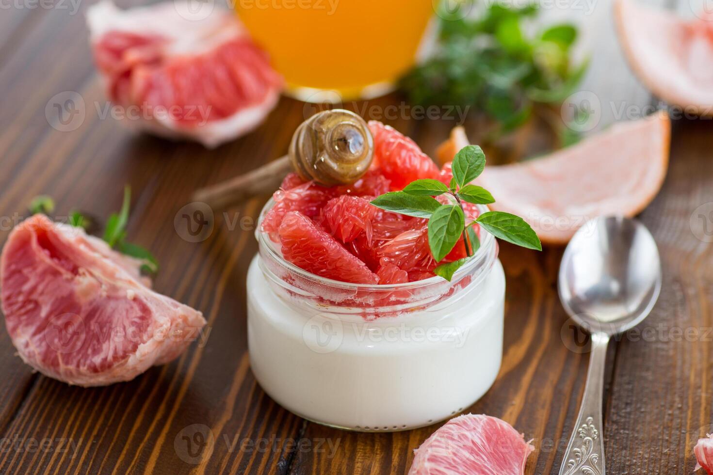 homemade sweet yogurt in a glass jar with pieces of red ripe grapefruit and honey, on a wooden table photo
