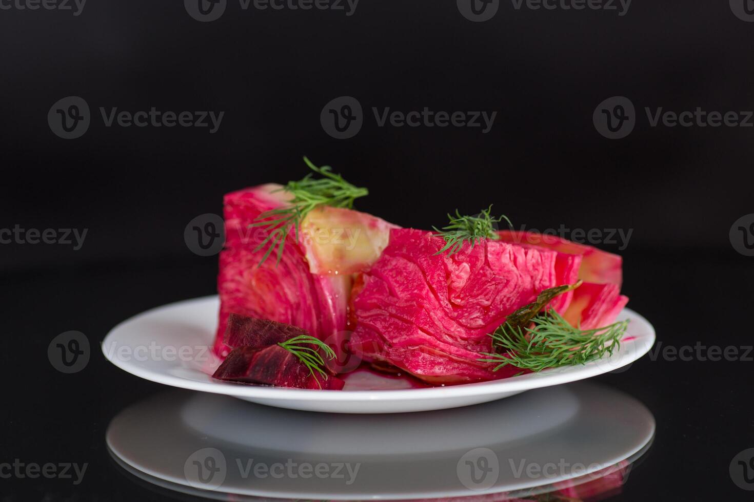 pickled cabbage with beets and carrots, in a plate, isolated on black background photo