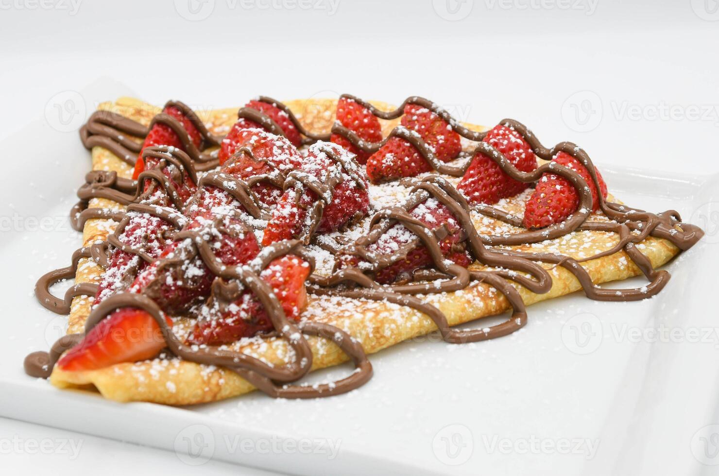 Crepe with strawberries and chocolate on a white plate. photo