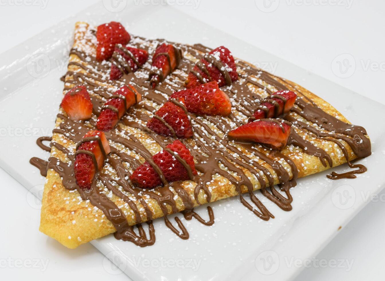 Crepe with strawberries and chocolate on a white plate. photo