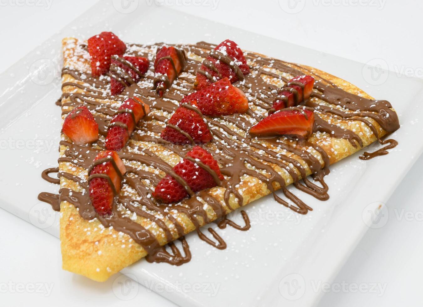 Crepe with strawberries and chocolate on a white plate. photo
