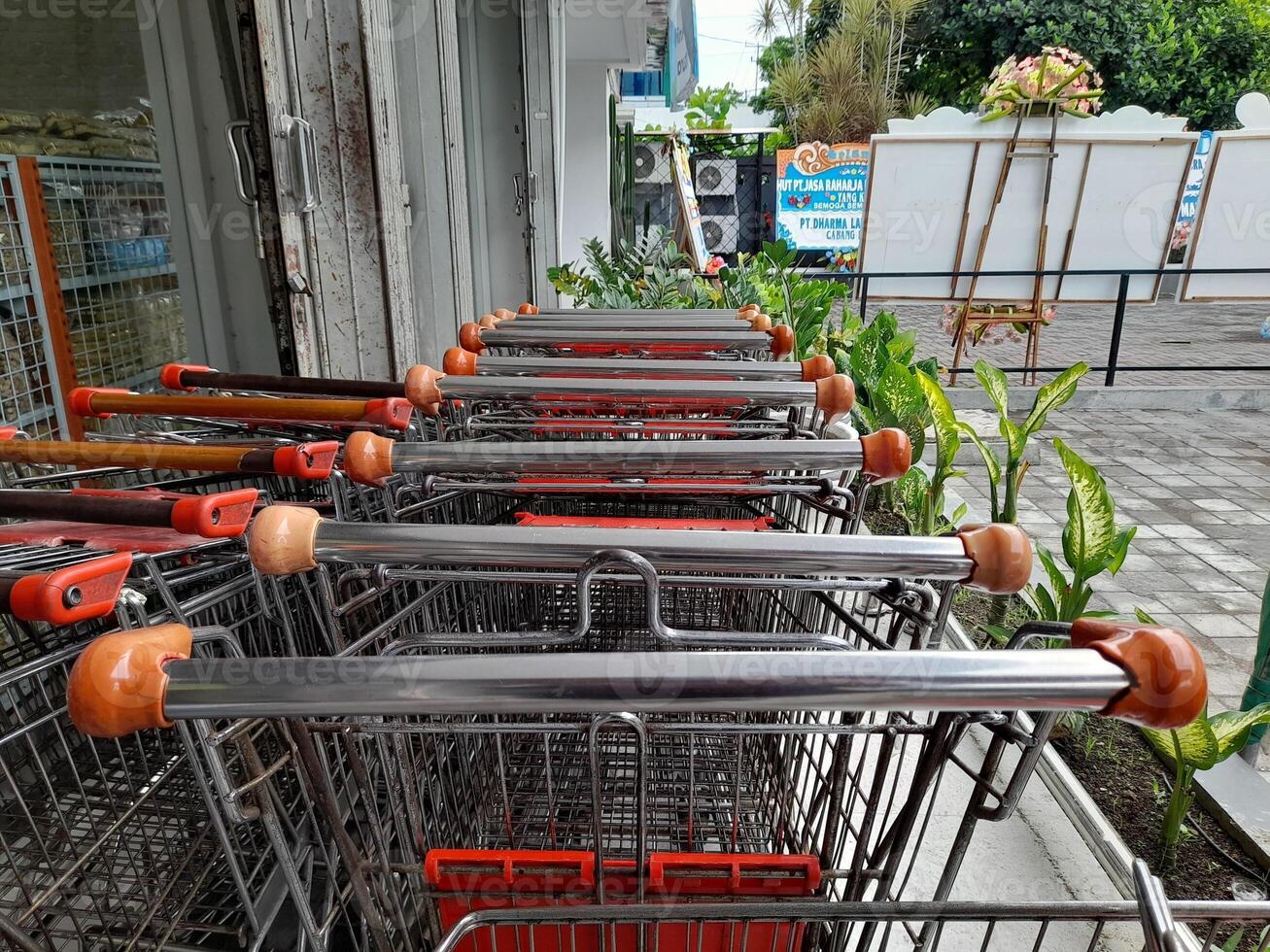 Mataram City, Indonesia - December 1, 2024. A row of shopping carts are neatly arranged outside a shop. The carts, made of metal with orange handles, are parked in an orderly fashion. photo