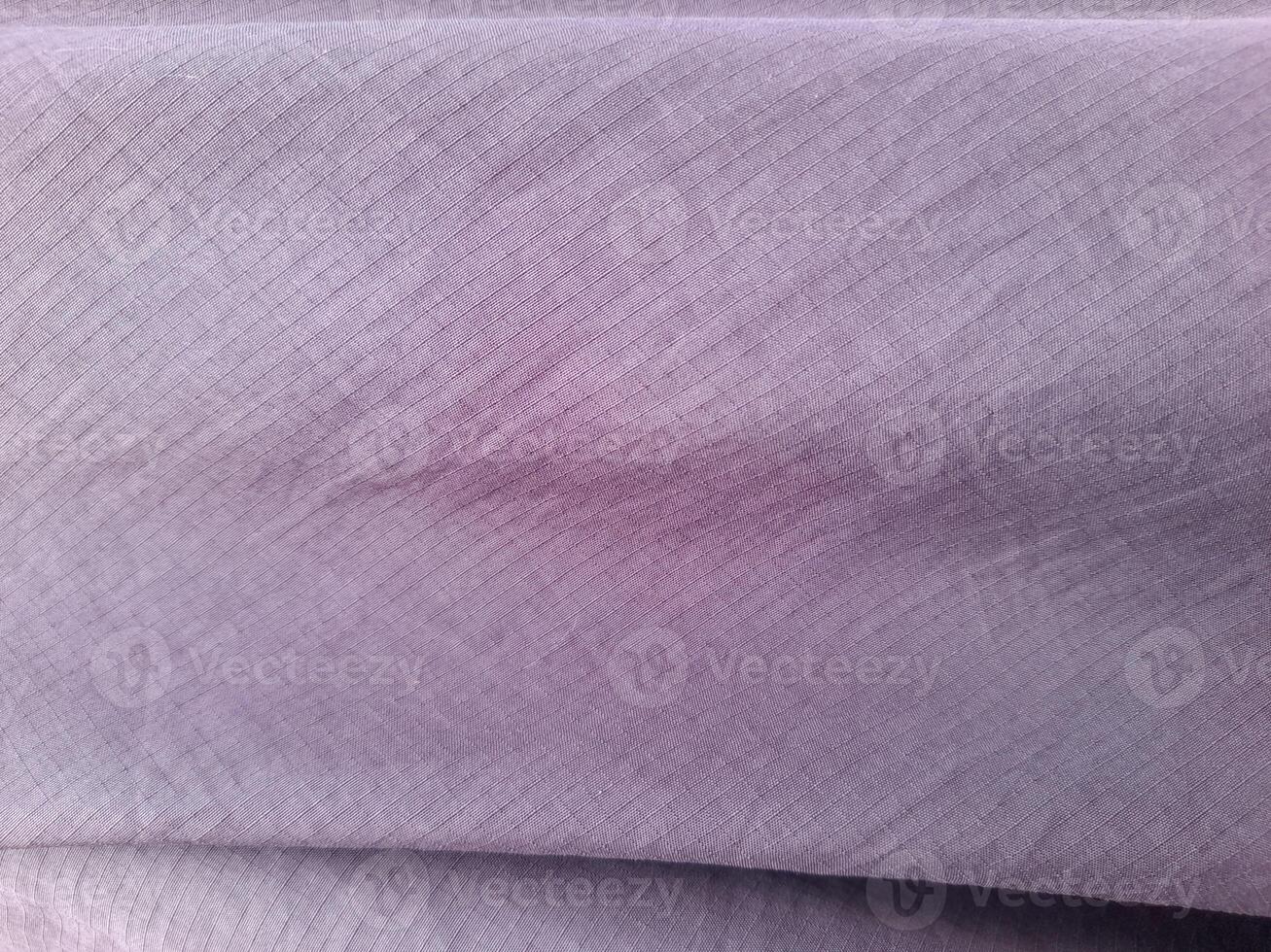 A close-up view of a light purple fabric with a fine, diagonal line pattern. The surface appears soft and smooth, with subtle folds that create a gentle texture, ideal for garments or home decor. photo