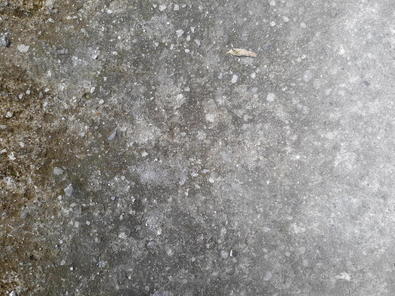 a close-up view of a weathered concrete surface. The concrete is predominantly gray in color, with a rough and uneven texture. photo