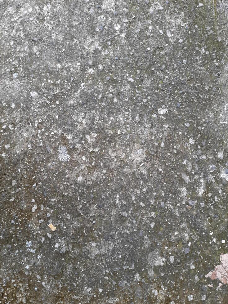 a close-up view of a weathered concrete surface. The concrete is predominantly gray in color, with a rough and uneven texture. photo
