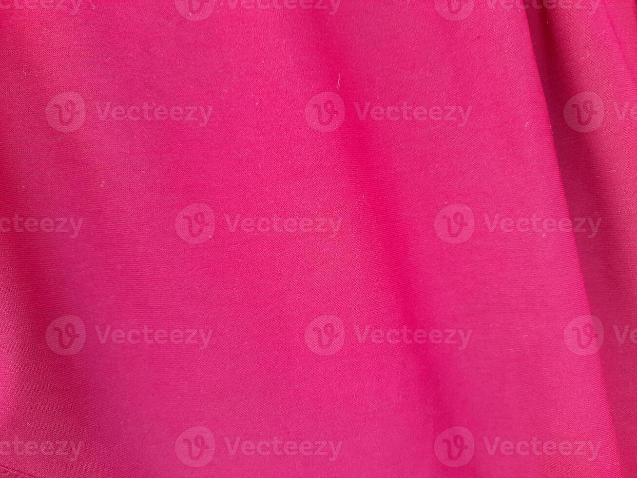 A close-up view of vibrant pink fabric with a smooth and slightly textured surface. The image showcases a diagonal fold, highlighting the fabric's soft drape and rich color. photo