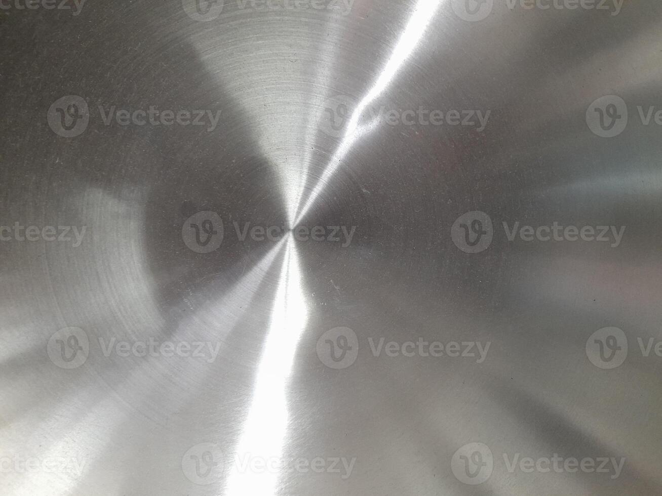 a close-up image of a brushed stainless steel surface. The circular brushing pattern is clearly visible, creating a textured appearance with fine lines radiating from the center. photo