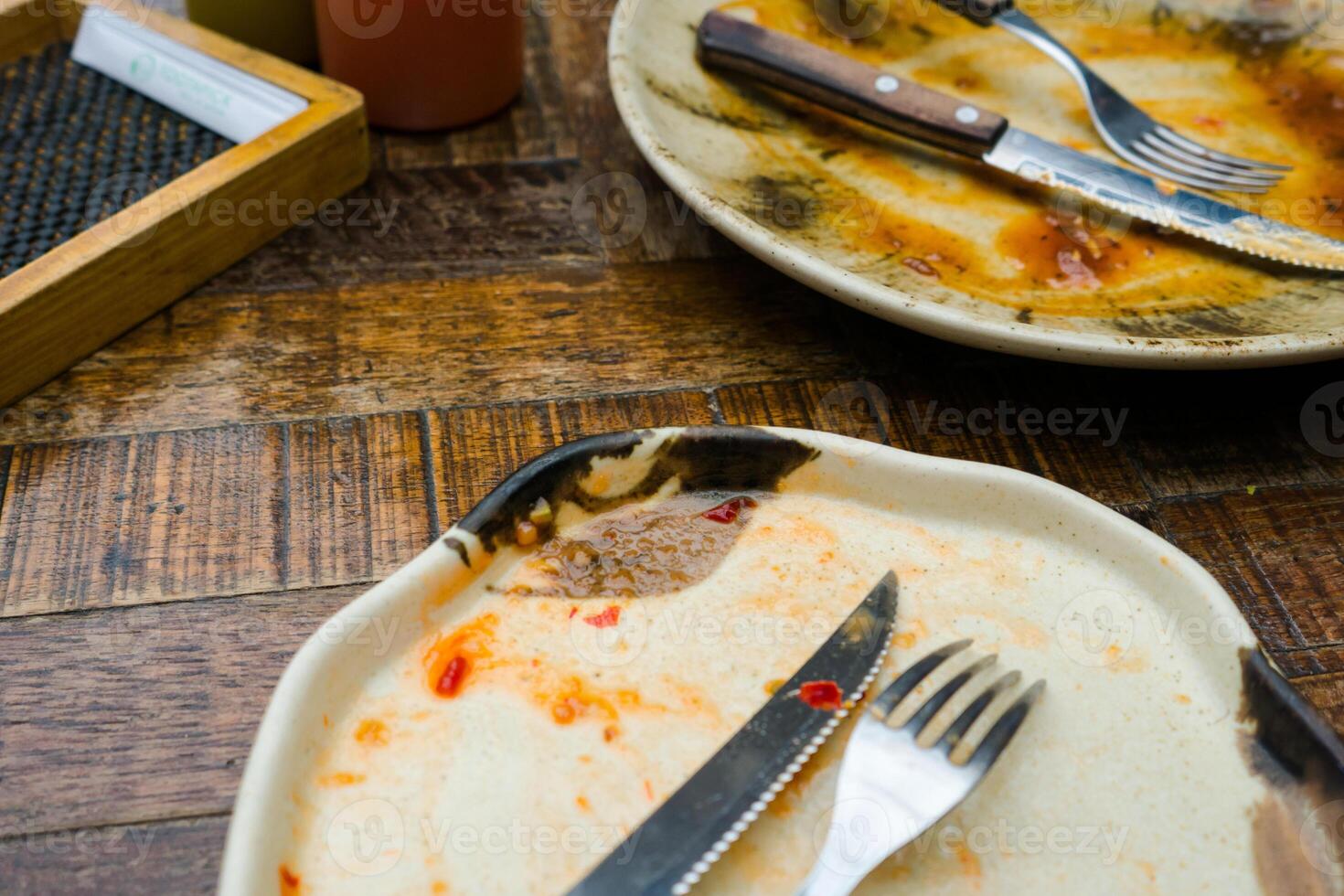 A cream-colored plate with a beautiful pattern shows leftover food, including a knife and fork. Some sauce remains on the plate, indicating the end of a meal photo
