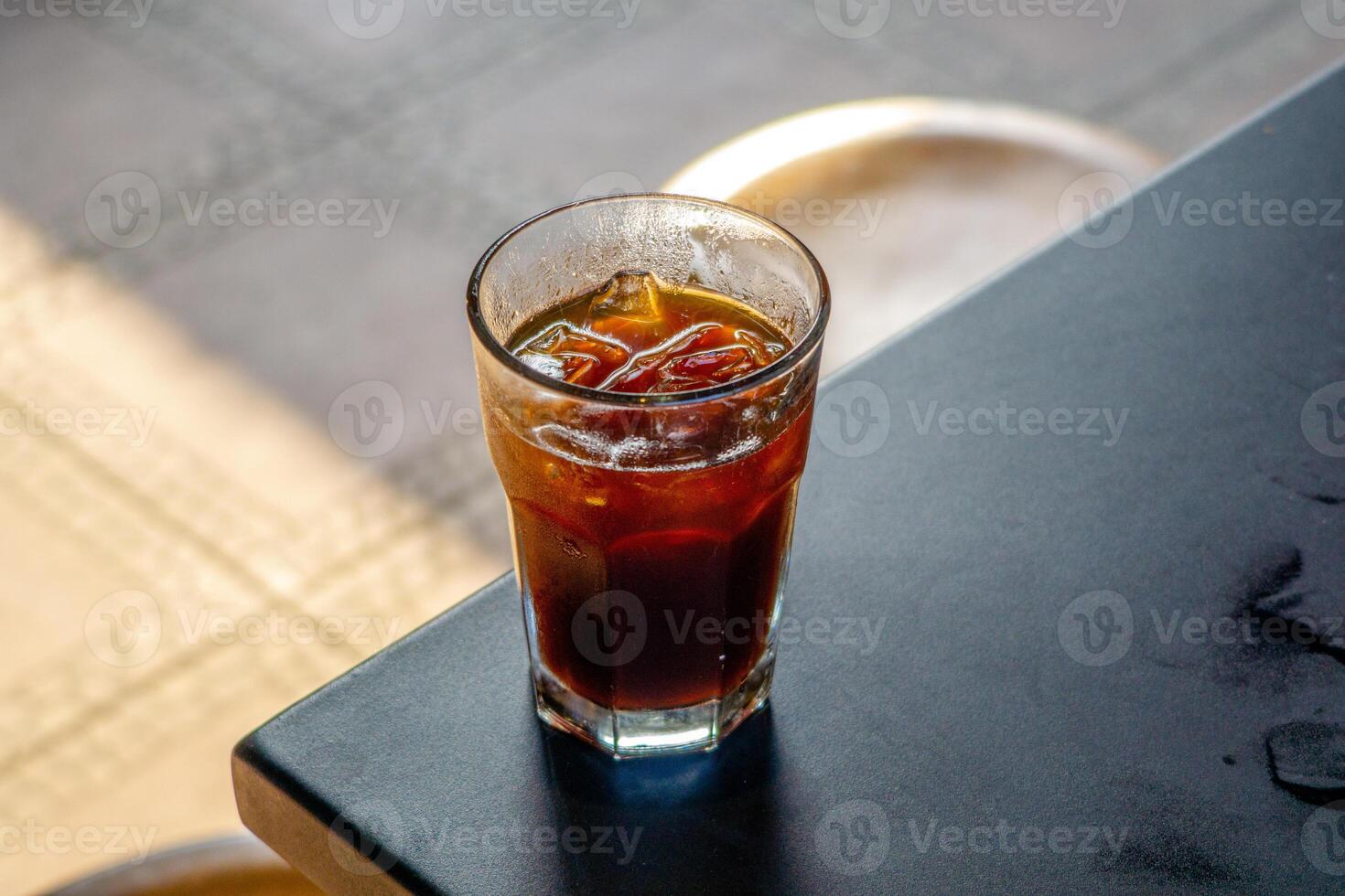 An iced americano served on a table at a coffee shop, with a cozy cafe ambience in the background. The cool beverage adds to the relaxed atmosphere of the cafe setting photo