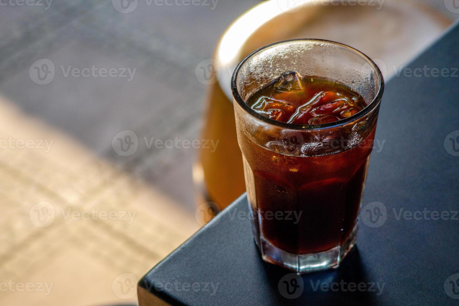 An iced americano served on a table at a coffee shop, with a cozy cafe ambience in the background. The cool beverage adds to the relaxed atmosphere of the cafe setting photo
