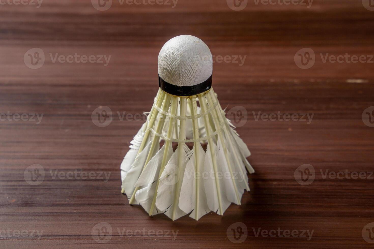 An isolated shuttlecock placed on a wooden table, showcasing its delicate feathers and intricate design. The simplicity of the scene highlights the shuttlecock details photo