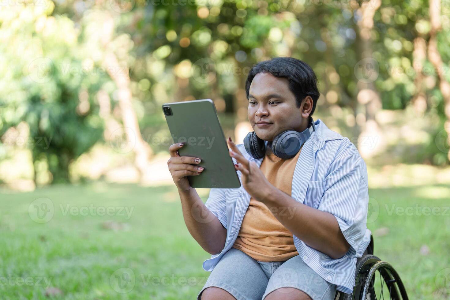 Young Man in Wheelchair Working Outdoors with Tablet and Headphones in a Garden Setting photo