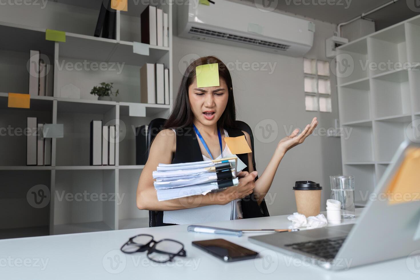Focused Businesswoman Multitasking at Desk with Documents, Laptop, and Coffee in Modern Office Environment photo