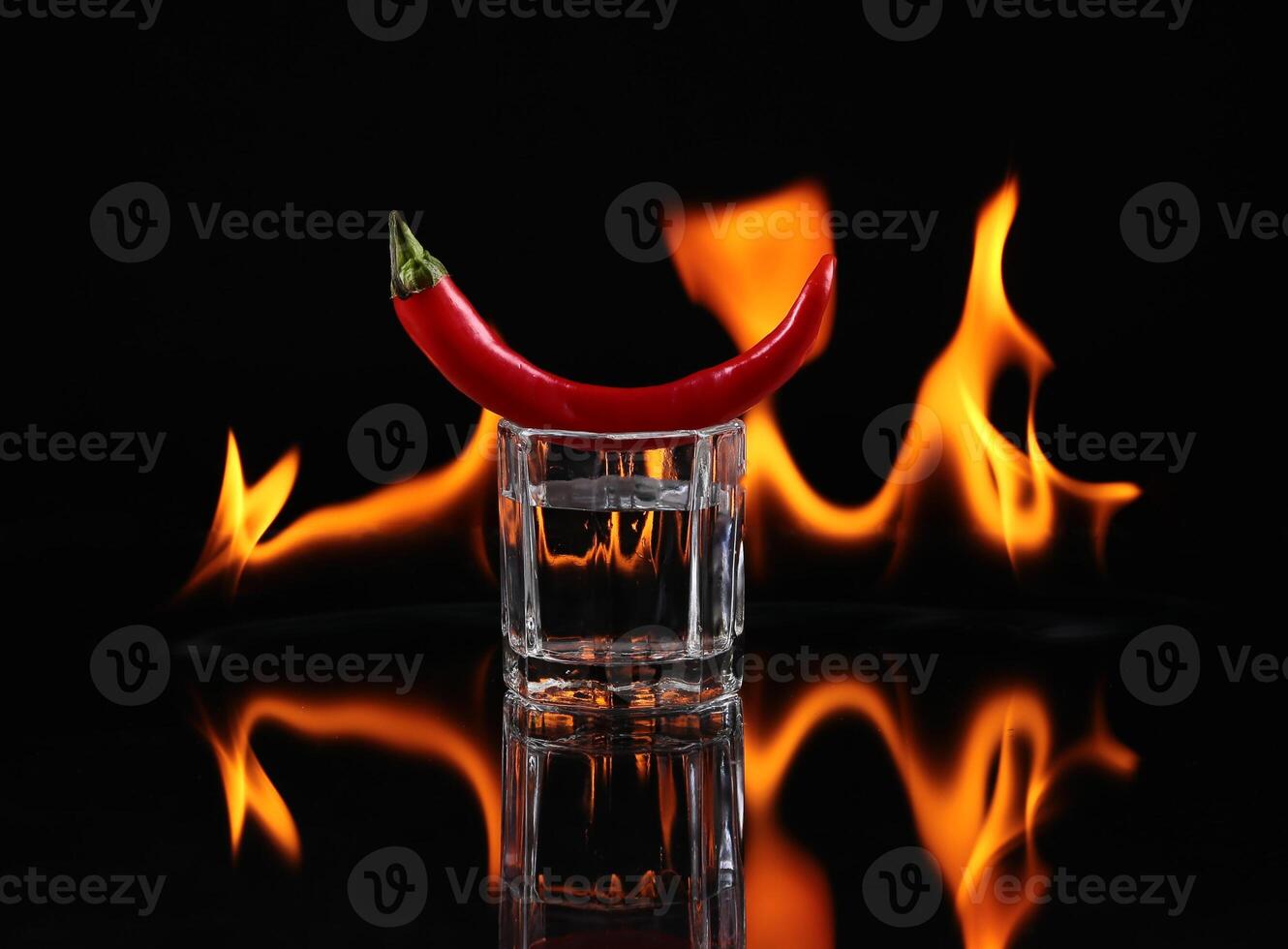 Hot chili pepper in a shot glass with a fire on a black background photo