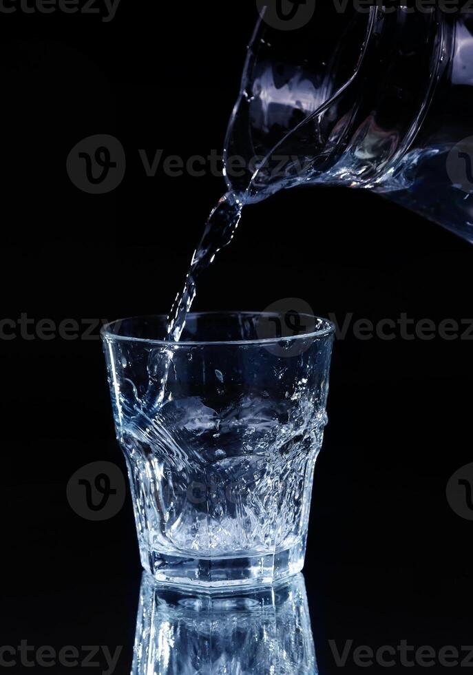 pouring water on a glass on black background photo