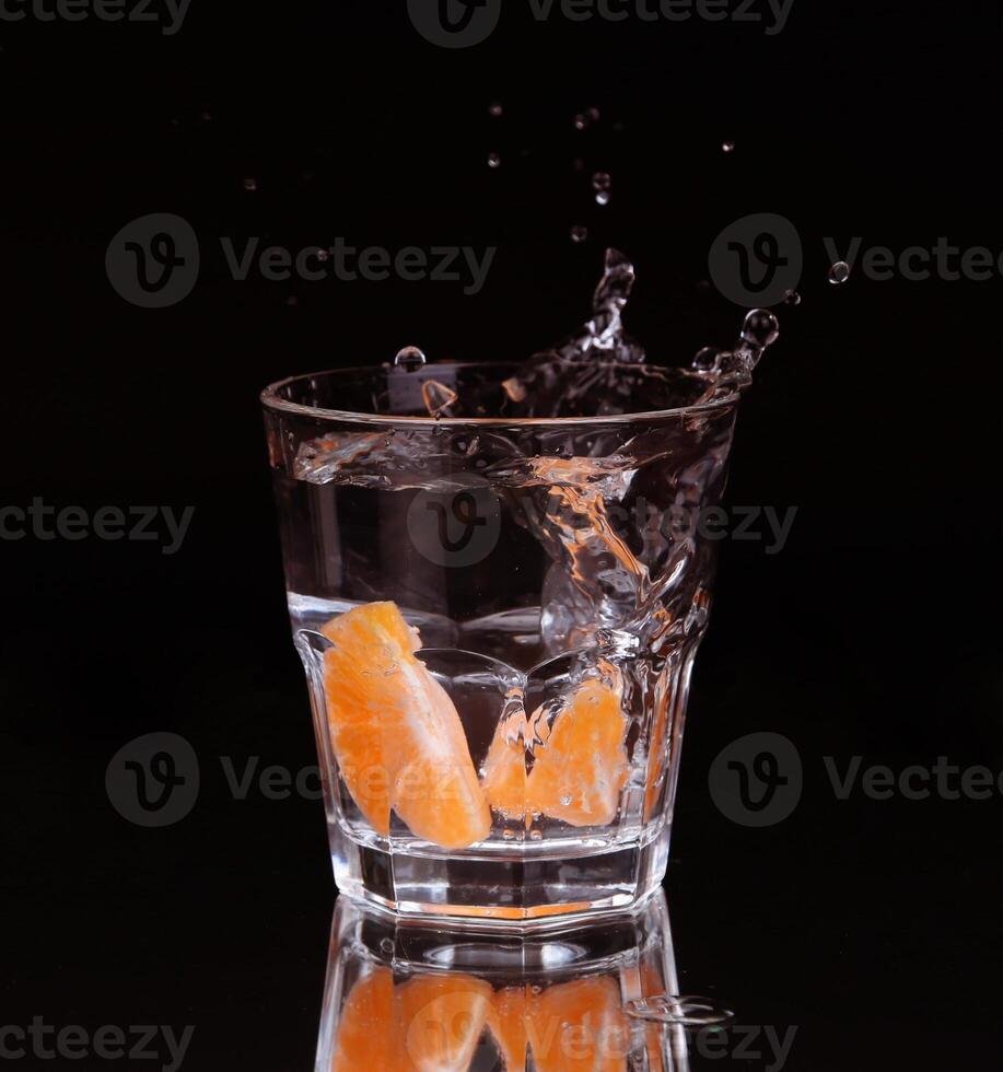 Slice of lemon splashing into a glass of water with a spray of water droplets in motion suspended in the air above the glass on a dark background. photo