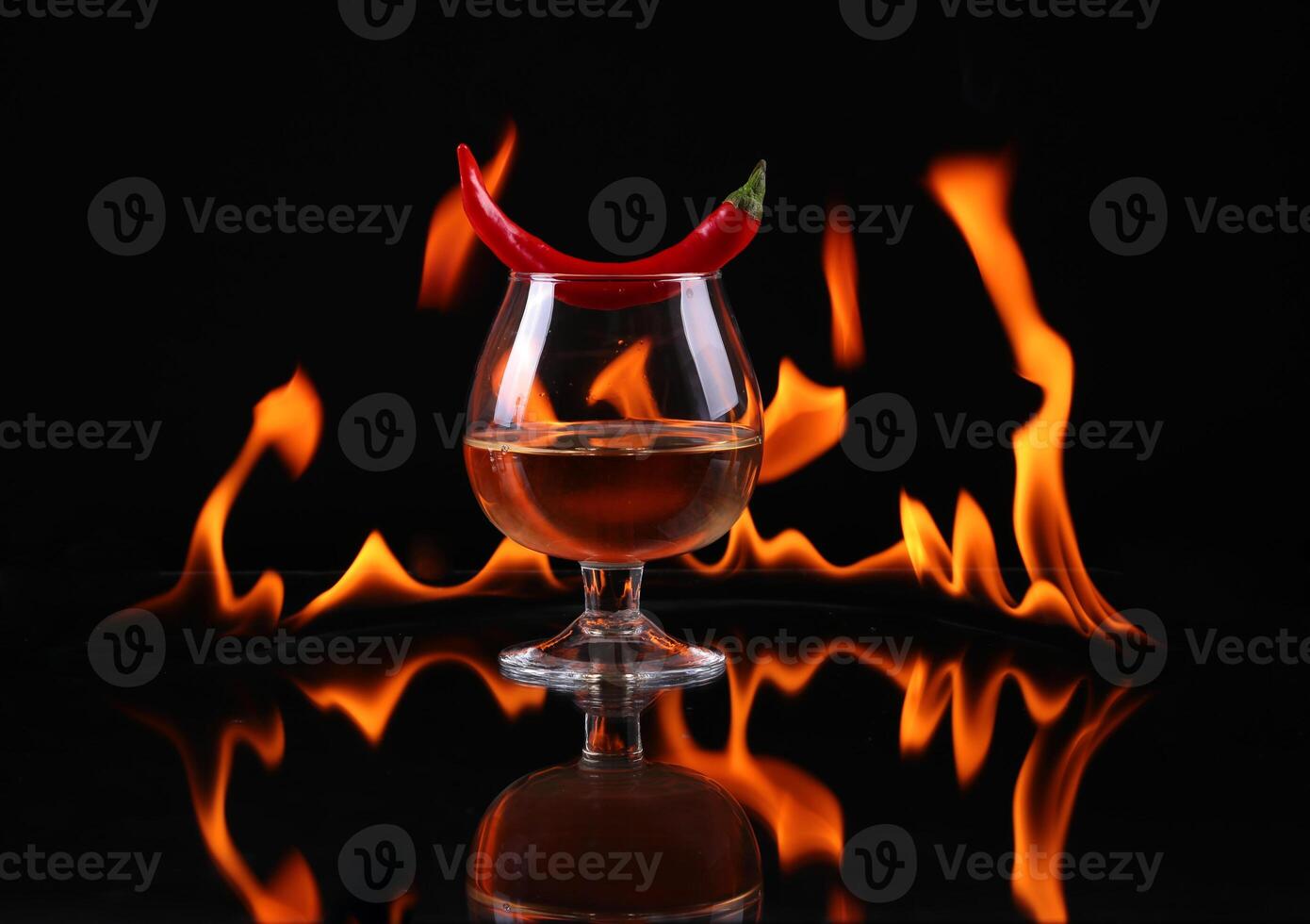 Hot chili pepper in a cognac ballon with a fire on a black background photo