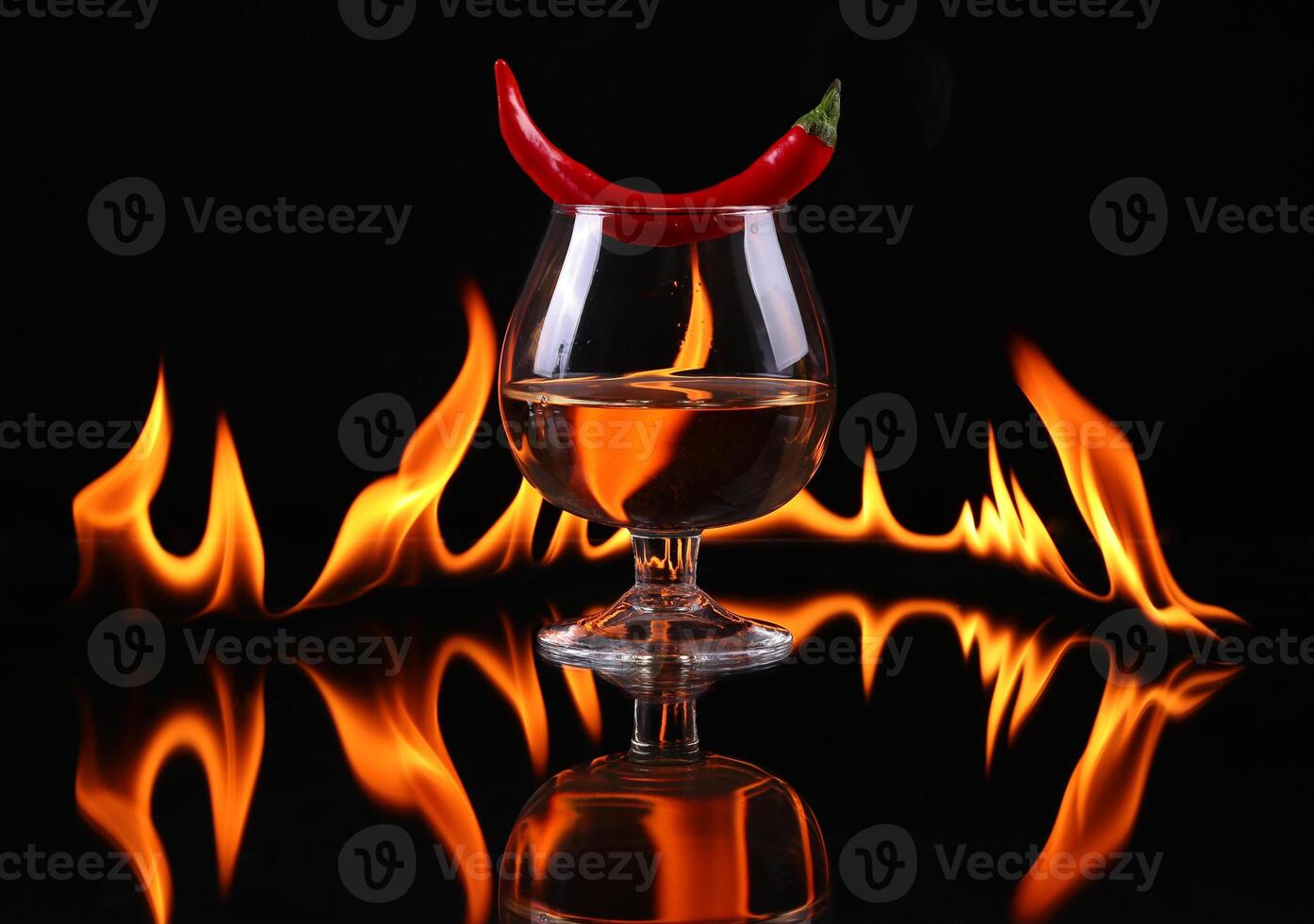 Hot chili pepper in a cognac ballon with a fire on a black background photo