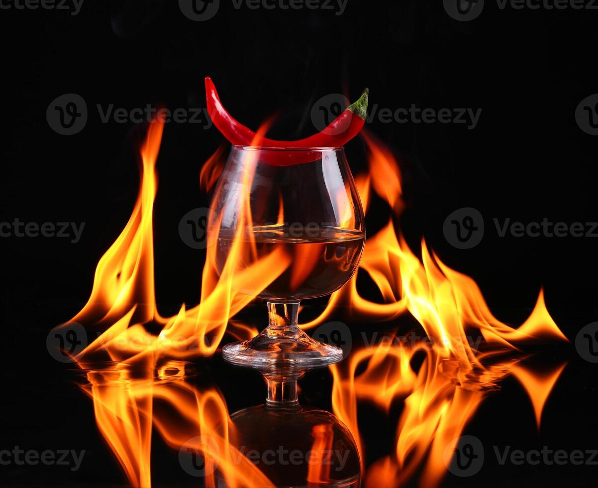 Hot chili pepper in a cognac ballon with a fire on a black background photo