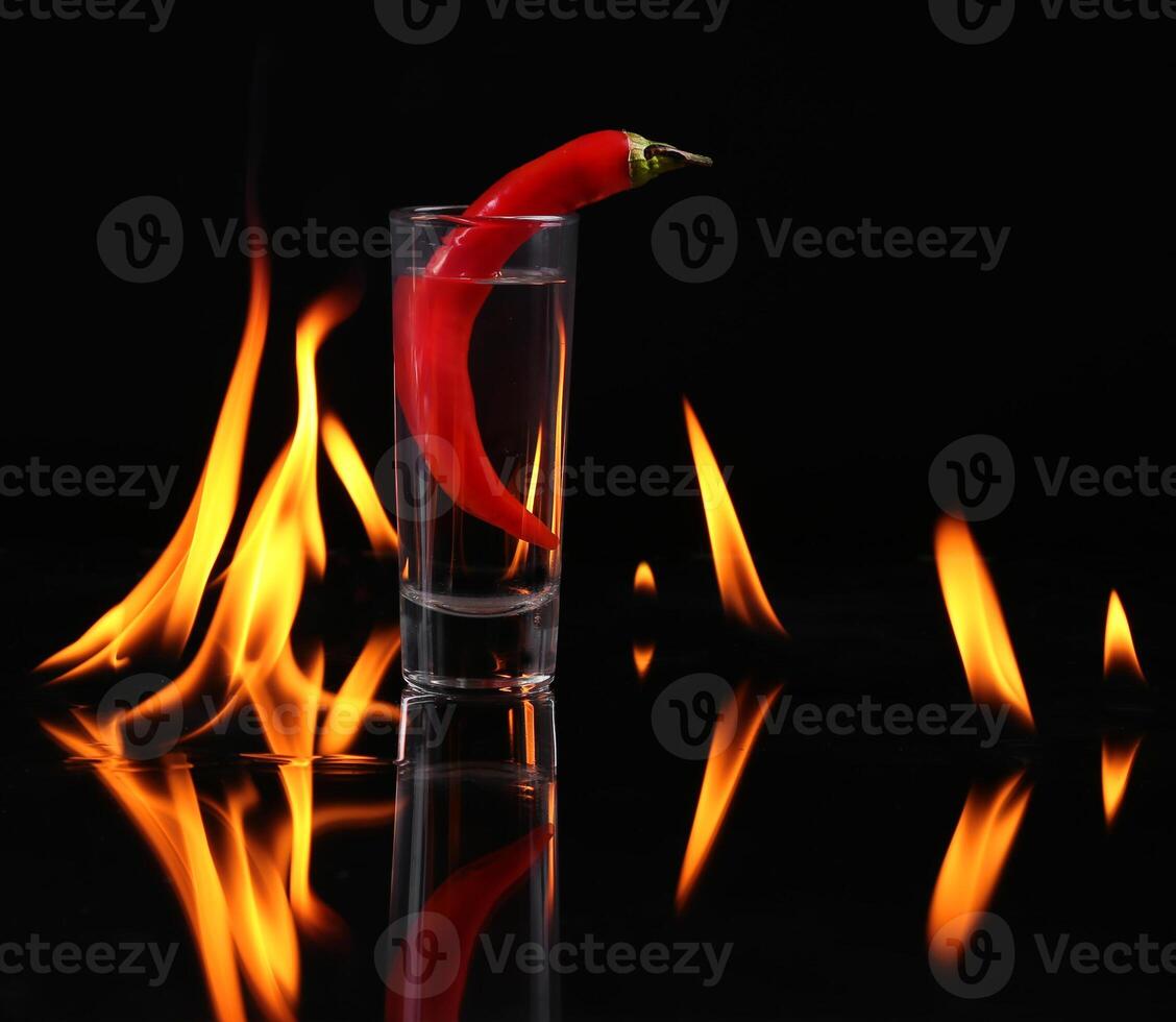 Hot chili pepper in a shot glass with a fire on a black background photo