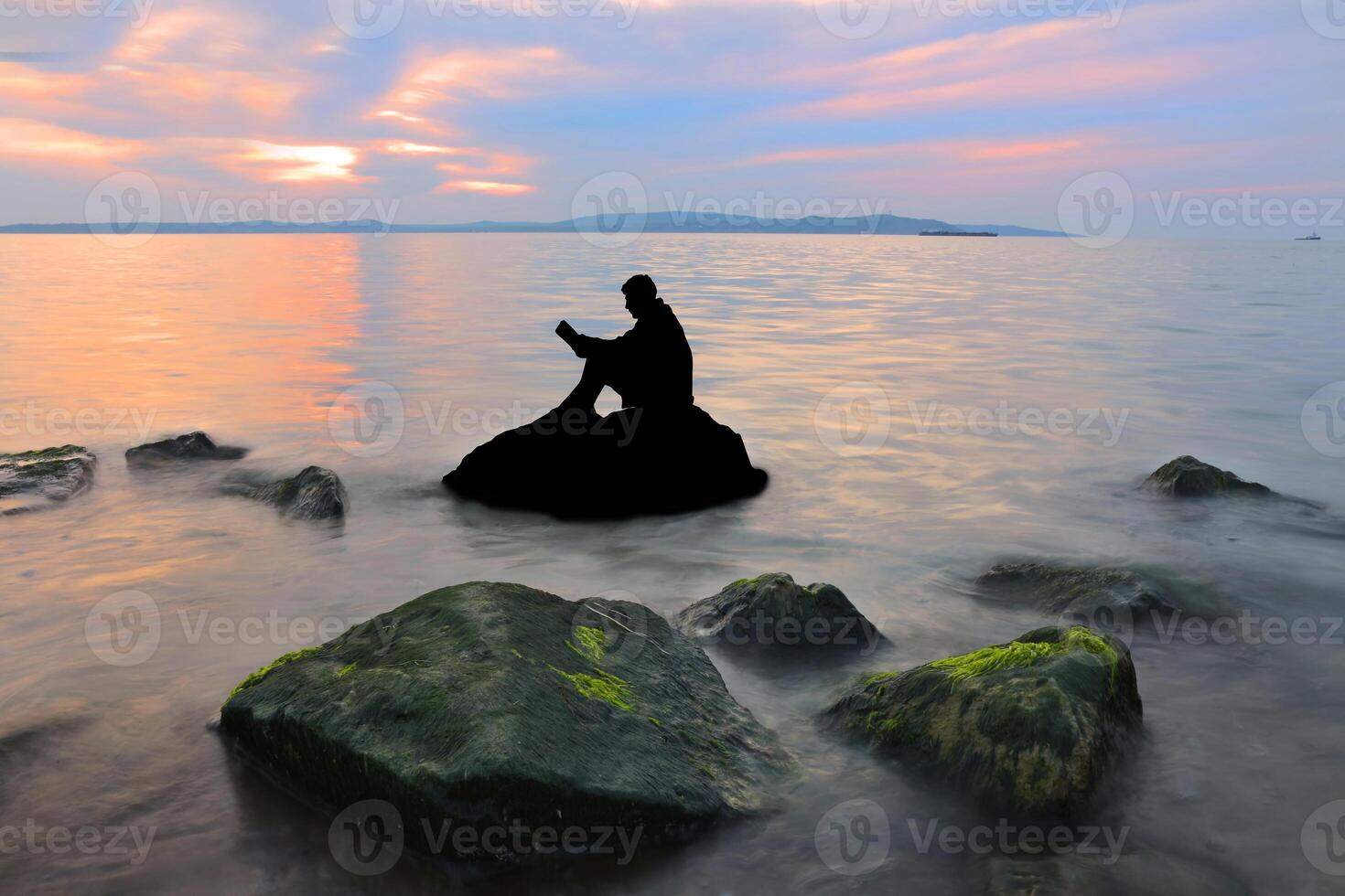 Silhouette guy sitting on breakwater in evening near sea, reads book photo