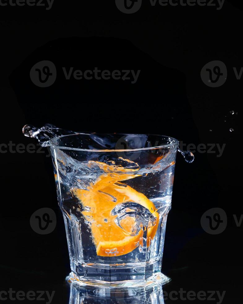 Slice of lemon splashing into a glass of water with a spray of water droplets in motion suspended in the air above the glass on a dark background. photo