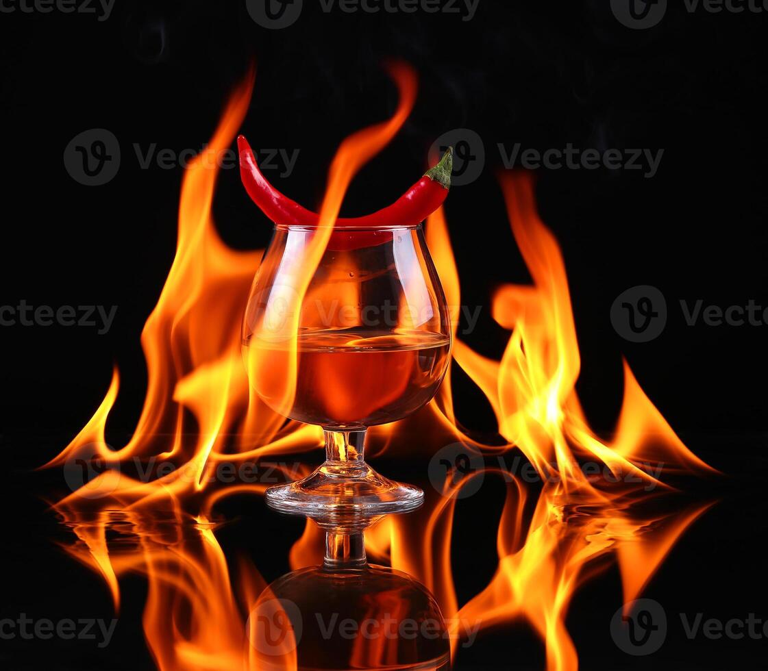 Hot chili pepper in a cognac ballon with a fire on a black background photo