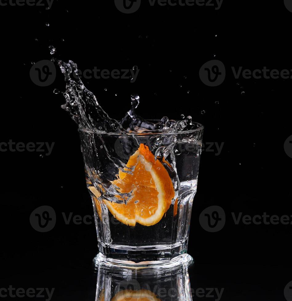 Slice of lemon splashing into a glass of water with a spray of water droplets in motion suspended in the air above the glass on a dark background. photo
